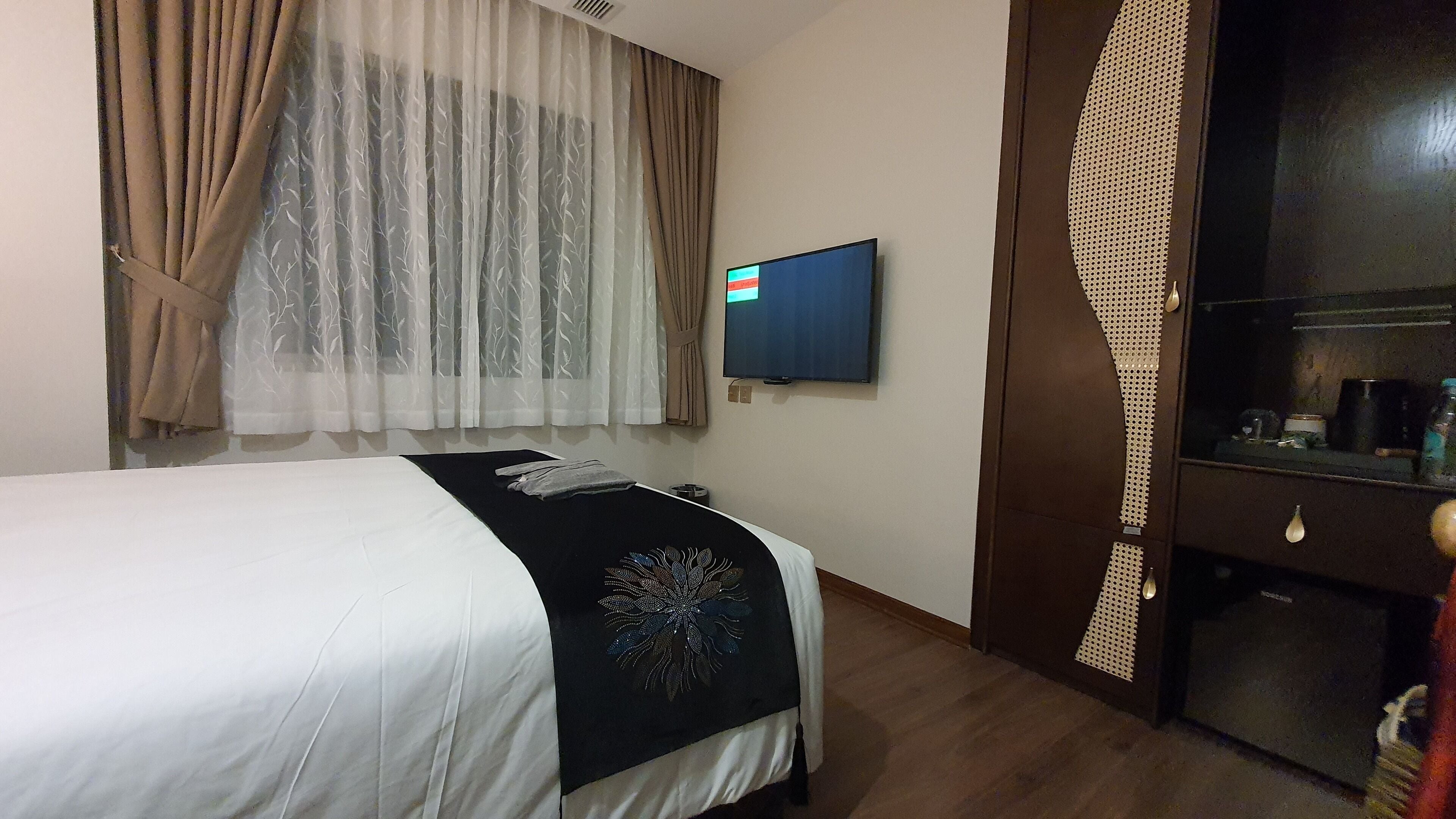 A hotel room with a bed, a television, a wardrobe, and a window with curtains.