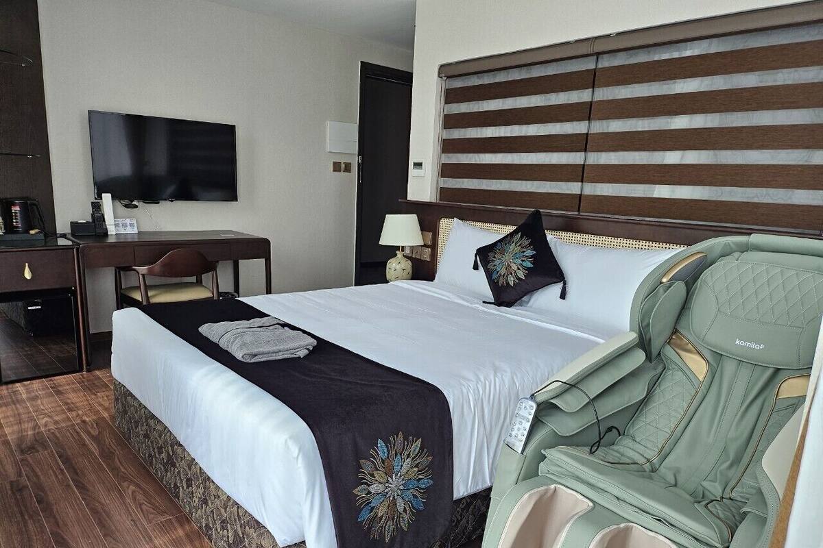 Una habitación de hotel con cama, escritorio, silla, televisor y ventana con persianas.