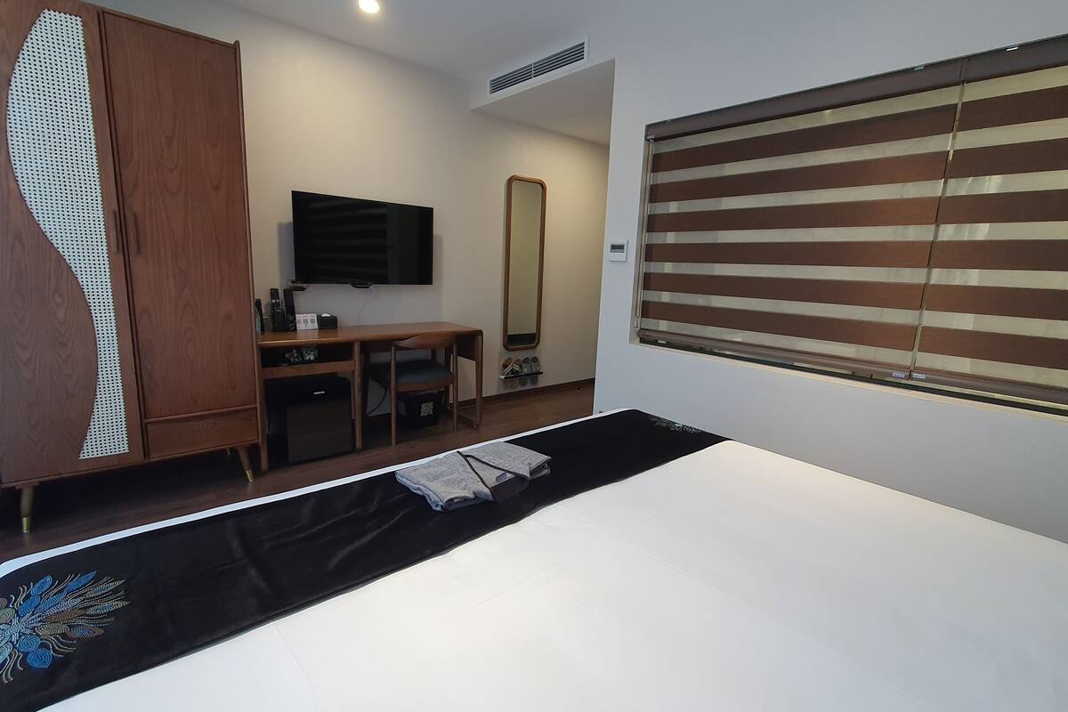 Una habitación de hotel con una cama, un escritorio, un armario, un televisor y una ventana con persianas.