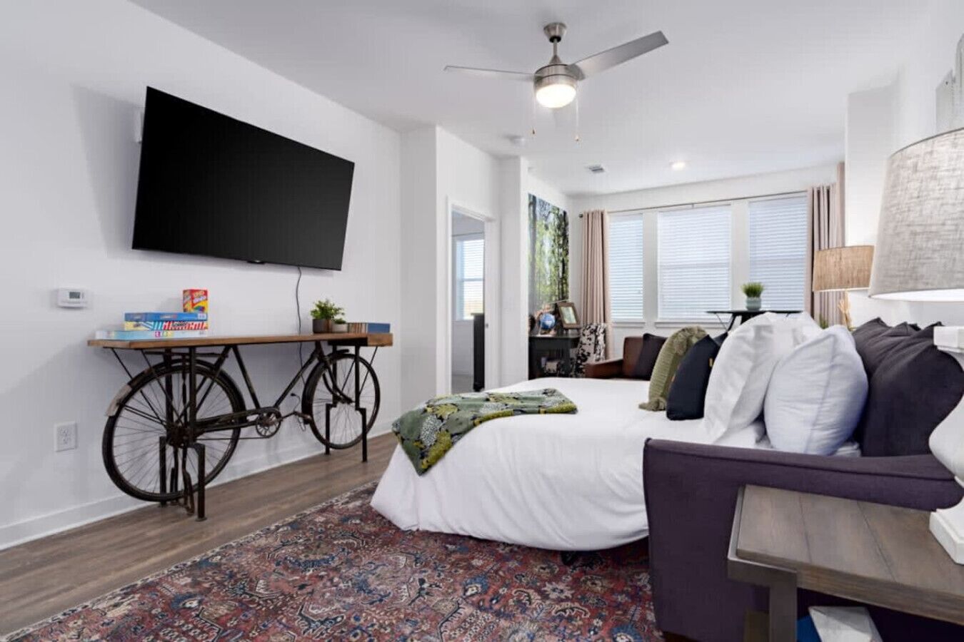 A modern, well-lit room with a bed, a sofa, a television mounted on the wall, and a bicycle as a unique furniture piece.