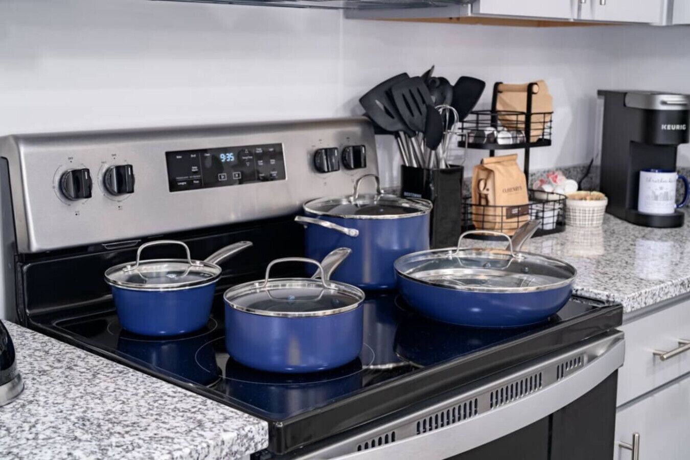 A kitchen with a stainless steel stove, three blue pots on the stove, and a coffee maker on the countertop.