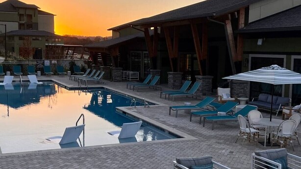 Un área de piscina con sillones de descanso y sombrillas, rodeada de edificios con construcciones de piedra y madera.