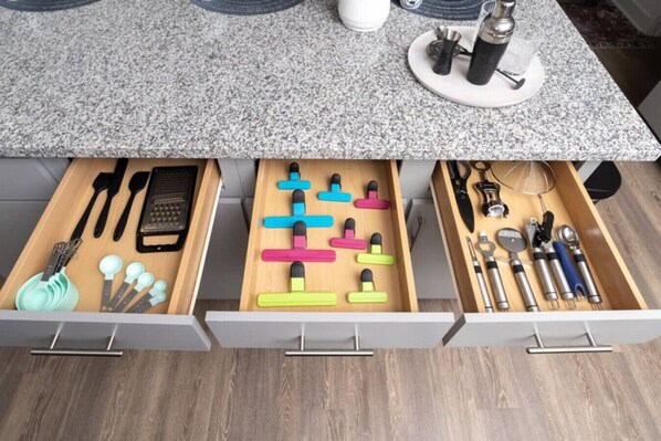 A kitchen with a granite countertop, wooden drawers, and various utensils.
