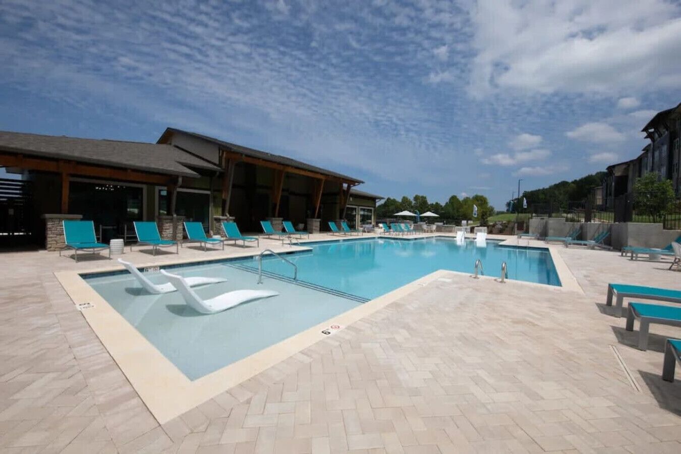 A rectangular swimming pool with a tiled deck, surrounded by lounge chairs and a covered seating area.