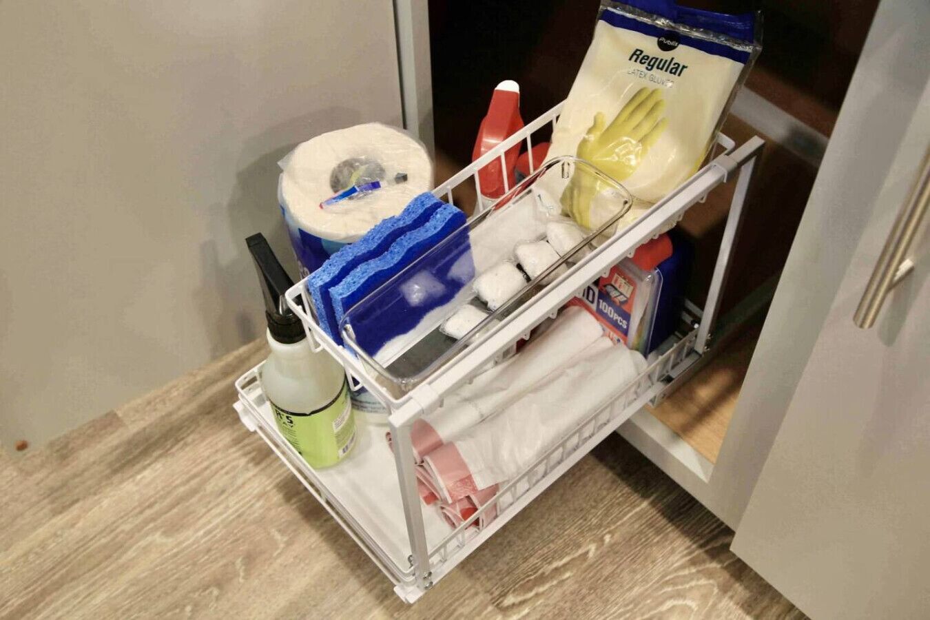 A storage cart with a toilet paper roll, a blue sponge, a bottle of hand soap, and a pack of tissues.
