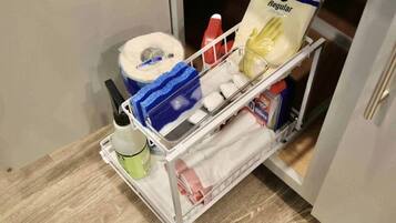 A storage cart with a toilet paper roll, a blue sponge, a bottle of hand soap, and a pack of tissues.