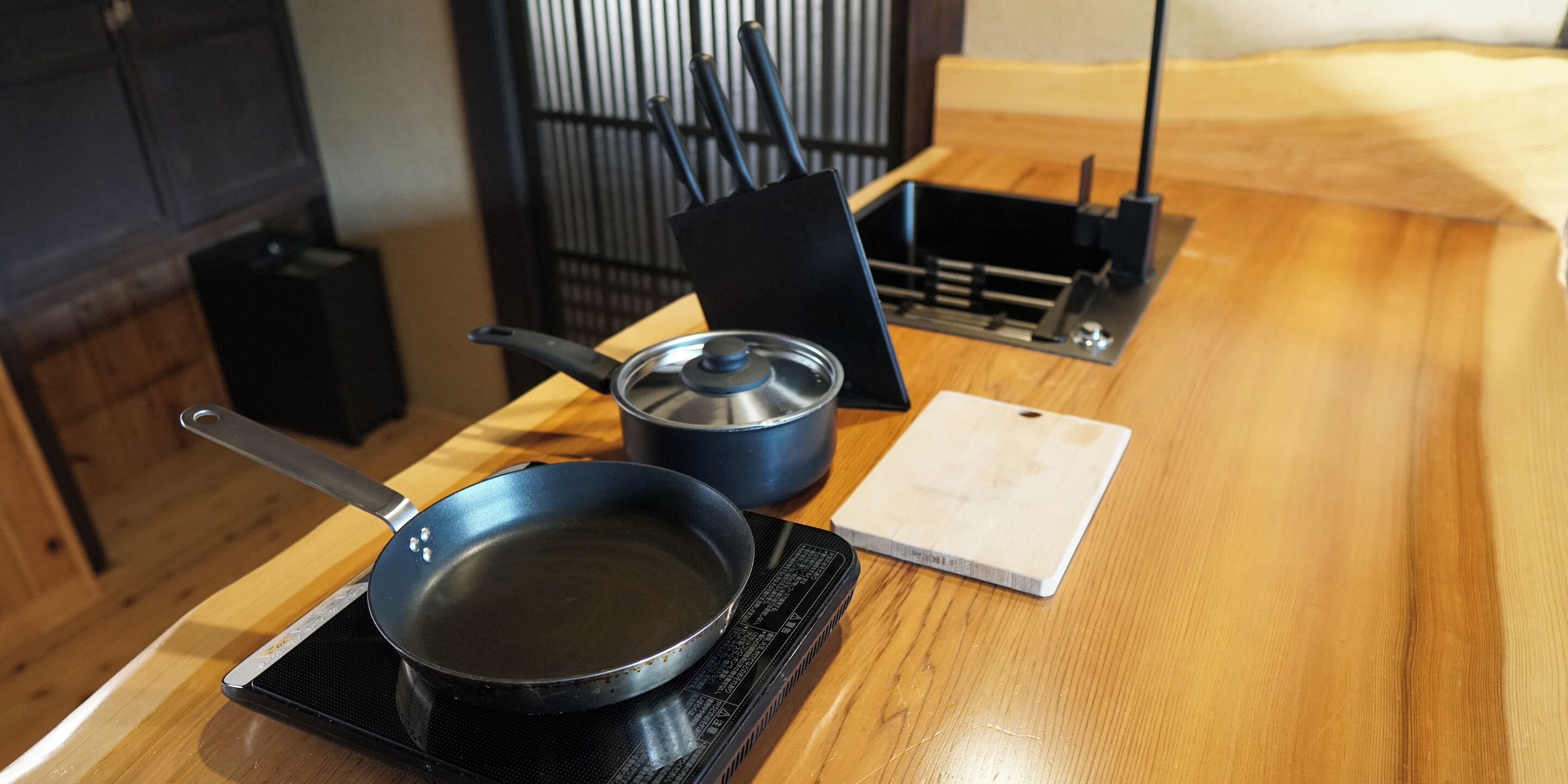Een keuken met een fornuis, een koekenpan, een pan en een snijplank op een houten tafel.