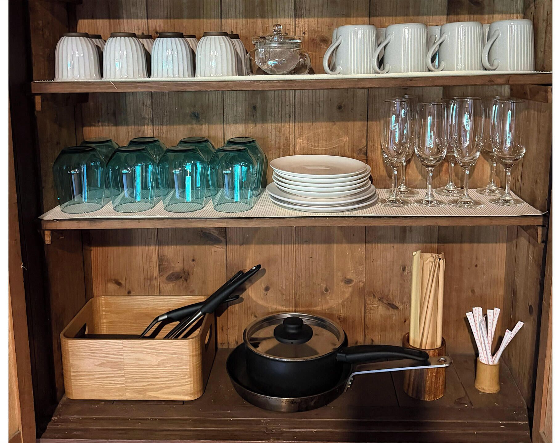 A wooden shelf with kitchenware, including glass jars, plates, and a frying pan.