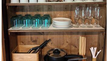 A wooden shelf with kitchenware, including glass jars, plates, and a frying pan.