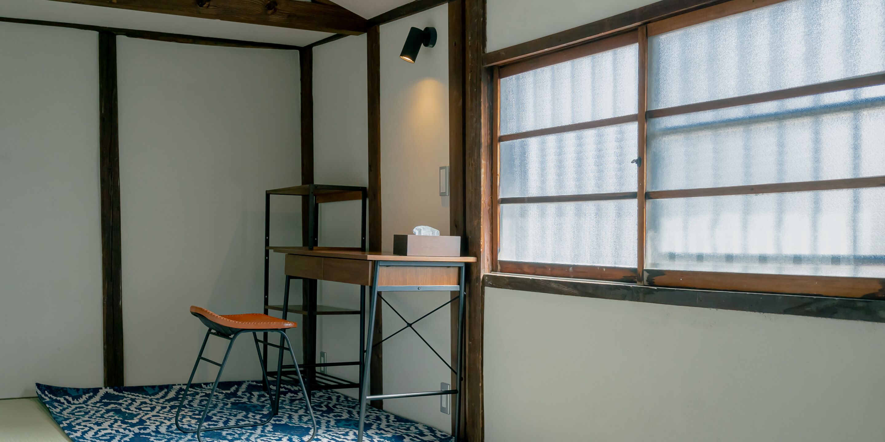 Una habitación con un escritorio de madera, un taburete y una ventana con vidrio esmerilado.
