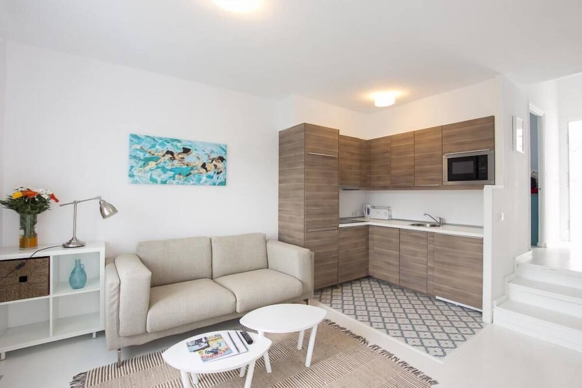 A compact living space with a kitchenette, a sofa, a coffee table, and a painting on the wall.