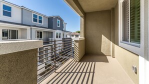 A balcony with a metal railing, beige walls, and a window with blinds. - Brand New 3b3b Condo in the heart of West Covina (West Covina)