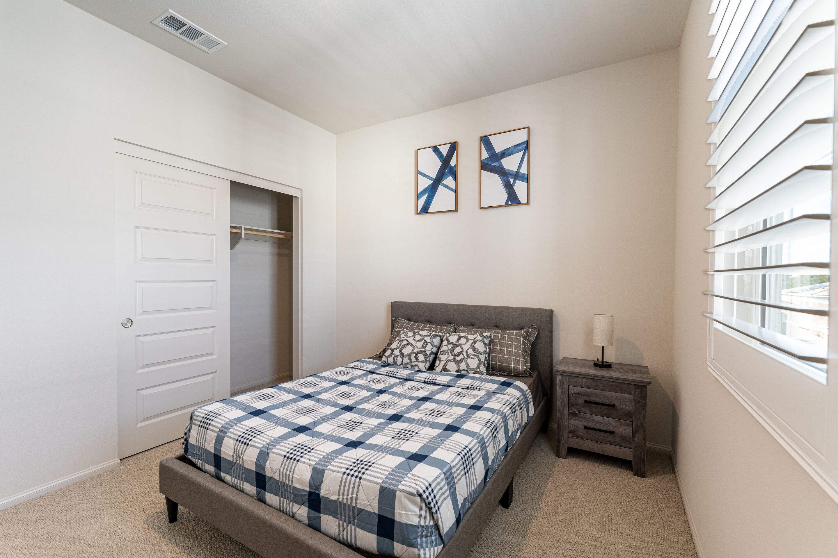 A bedroom with a bed, nightstand, and a window with blinds.