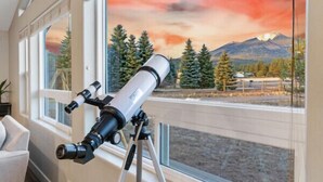 A telescope on a tripod in a room with large windows and a mural of a sunset landscape. - Large Groups, Volleyball Court, Large Space (Flagstaff)