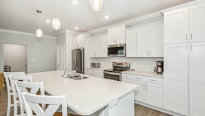 Une cuisine moderne avec des meubles blancs, des appareils en acier inoxydable et un îlot central doté de tabourets de bar.