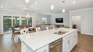 Une cuisine moderne dotée d’un grand îlot central, de meubles blancs, d’appareils électroménagers en acier inoxydable et de luminaires suspendus.