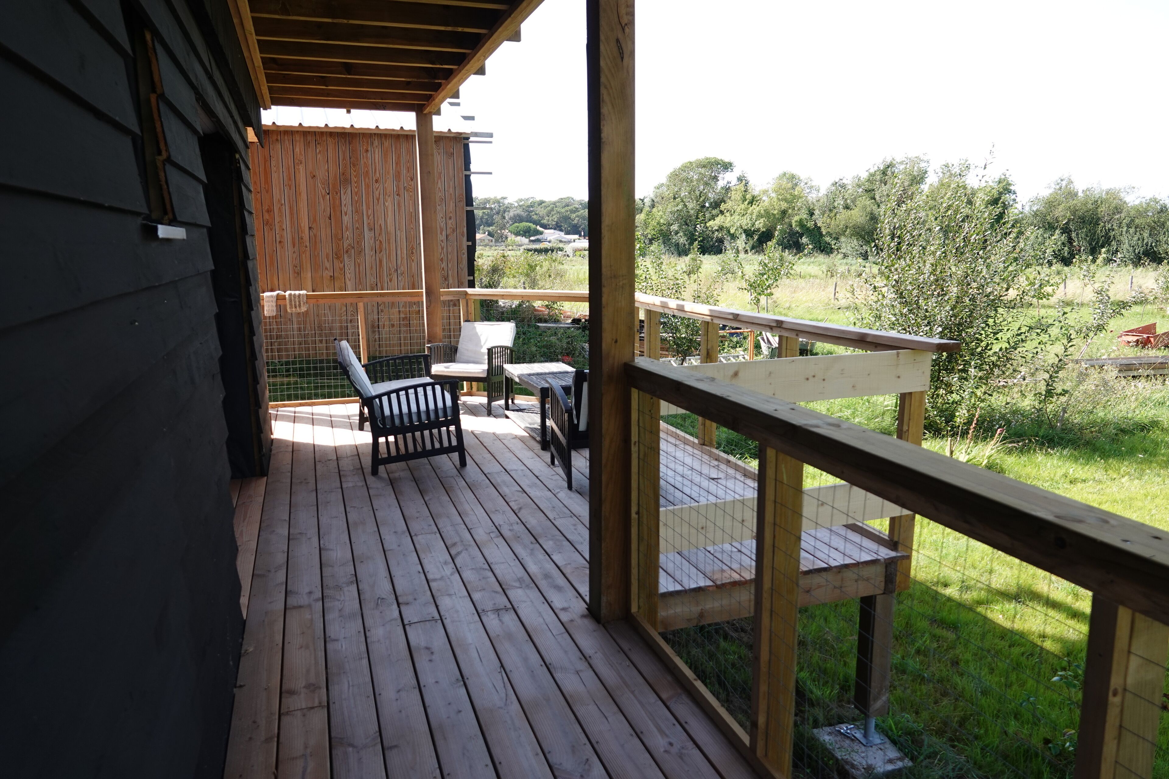 Una terraza de madera con una mesa y sillas, con vista a un área verde con árboles.