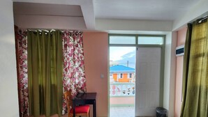 Una habitación con cama, una mesita con silla, una ventana con cortinas y vistas a edificios.