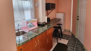 Una cocina compacta con fregadero, encimera, armarios, microondas, refrigerador y un taburete pequeño.