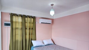 Un dormitorio con cama, cortinas, aire acondicionado y lámpara en el techo.