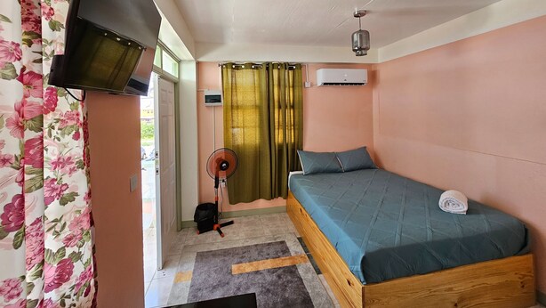 Un dormitorio con cama, ventilador, aire acondicionado y ventana con cortinas.