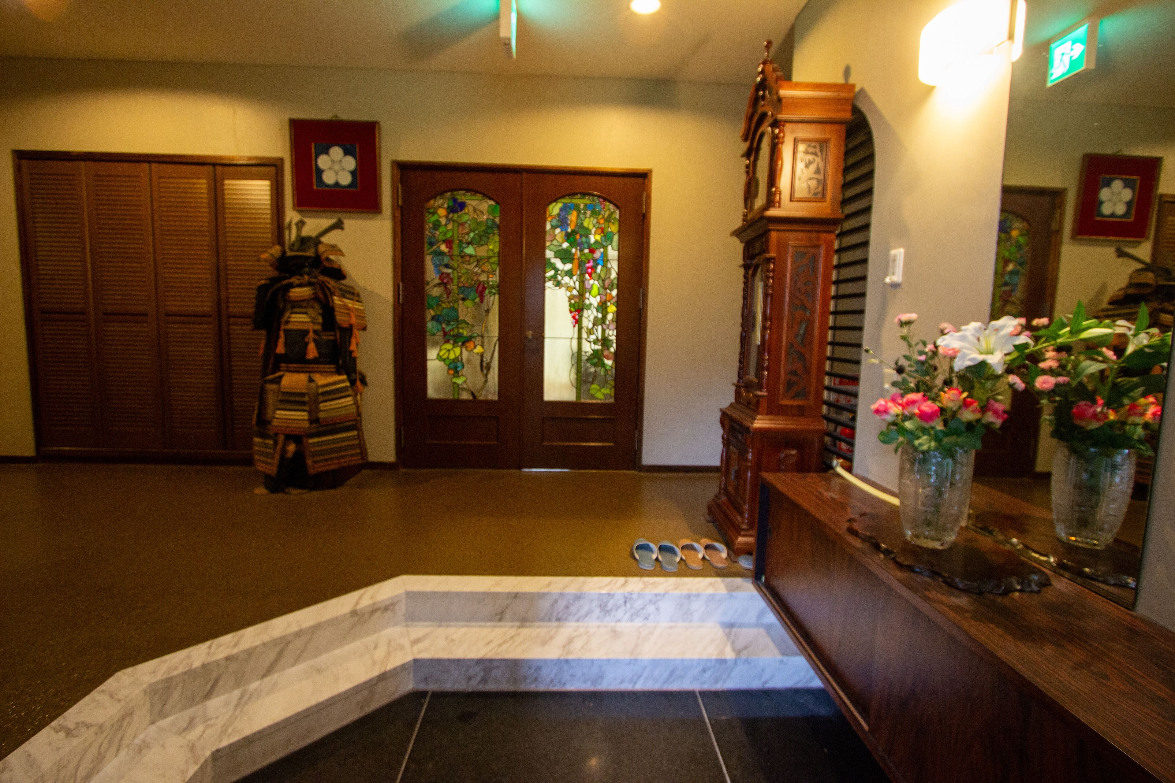 A hotel lobby with a marble staircase, wooden doors, and a reception desk with a vase of flowers.