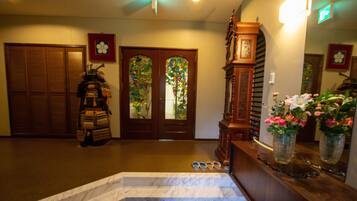 A hotel lobby with a marble staircase, wooden doors, and a reception desk with a vase of flowers.