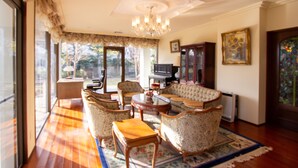 A spacious living room with a chandelier, comfortable seating, a television, and a large window offering a view of the outdoors. - HOTEL DO-YA BEPPU Hanare (Beppu)
