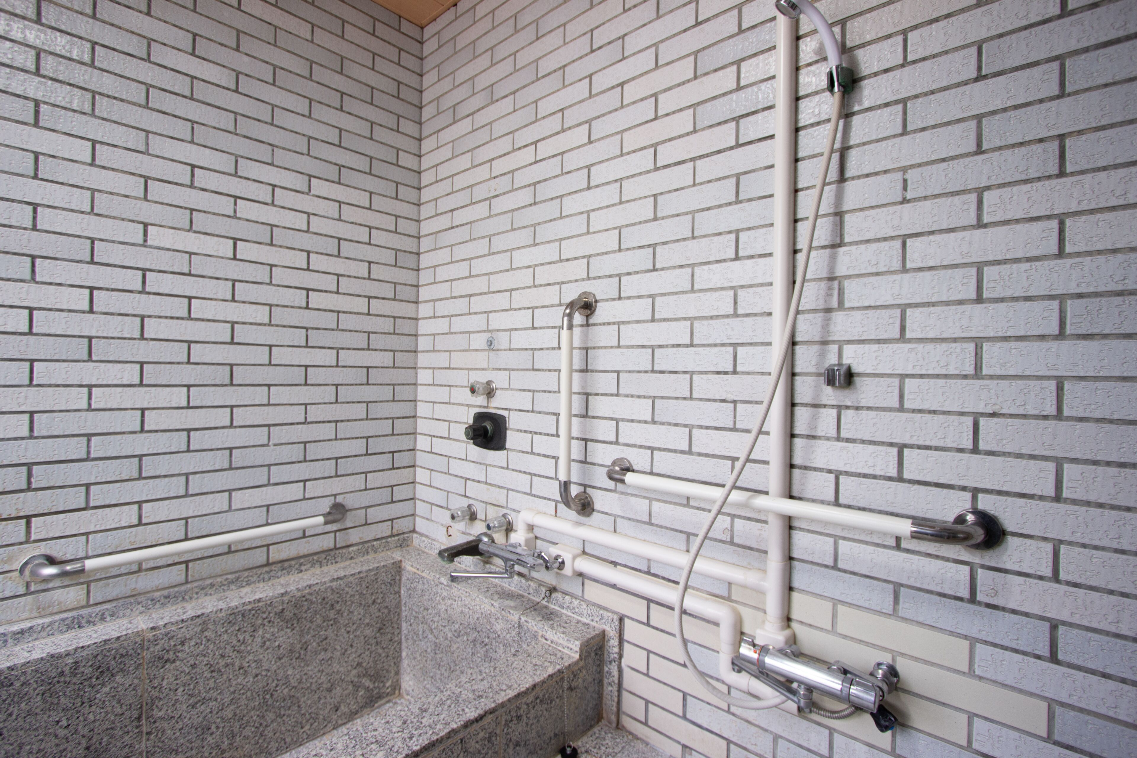 A bathroom with white brick walls, a granite bathtub, and modern fixtures including a handheld showerhead and a handheld faucet.