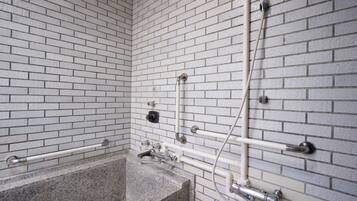 A bathroom with white brick walls, a granite bathtub, and modern fixtures including a handheld showerhead and a handheld faucet.