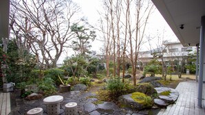 A stone pathway leading to a seating area with three stools, surrounded by rocks and greenery. - HOTEL DO-YA BEPPU Hanare (Beppu)