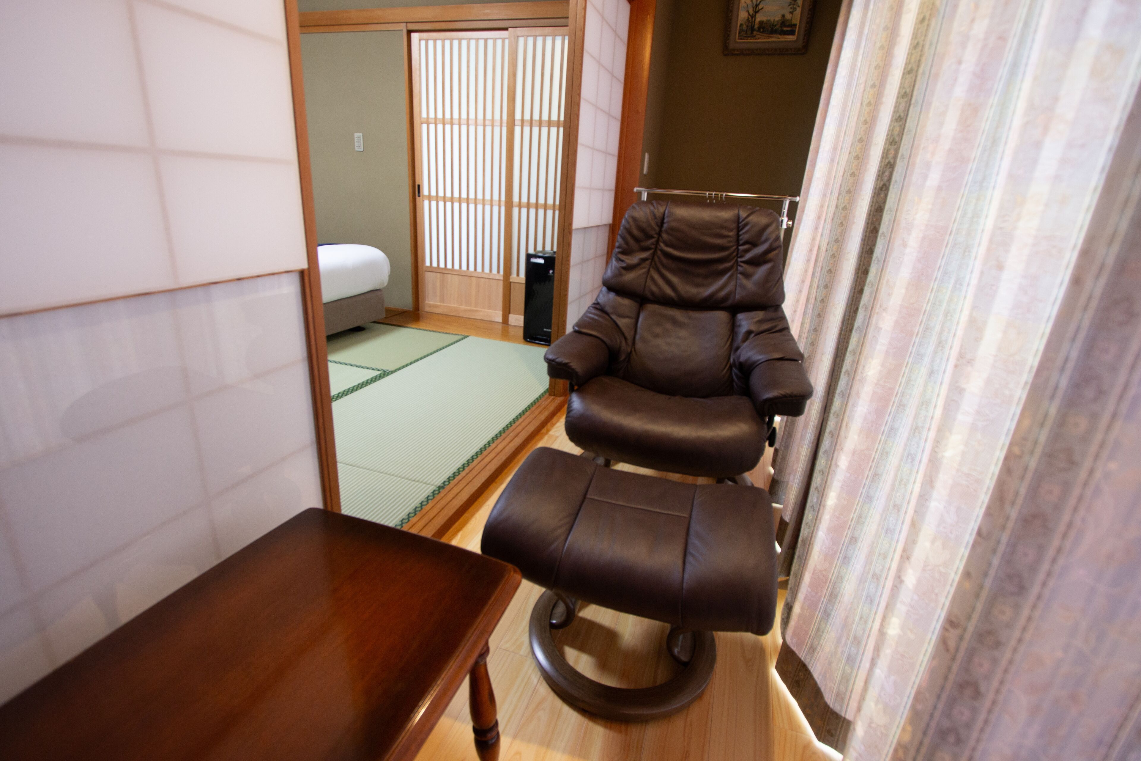 A traditional Japanese room with tatami flooring, a wooden table, a leather chair, and a sliding shoji screen.