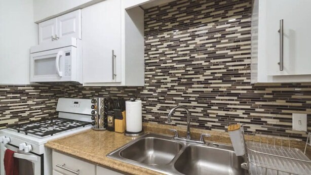 Una cocina moderna con gabinetes blancos, un lavamanos de acero inoxidable, un microondas y una estufa a gas.