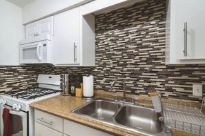 A modern kitchen with white cabinets, a gas stove, a microwave, a double sink, and a patterned backsplash.
