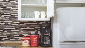 Una cocina con cafetera, café Folgers y un tarro de crema de café sobre la encimera.