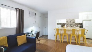 Una sala moderna con un sofá azul, un comedor con sillas amarillas y una cocina al fondo.