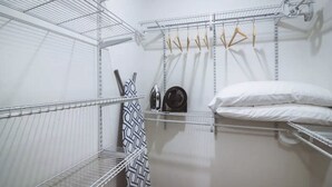 Un vestidor con estantes metálicos, una cama con ropa blanca y prendas colgadas en un perchero.