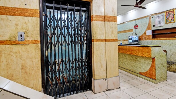 A reception area with a tiled floor, a reception desk, a television, and a calendar on the wall. - Hotel Dinar (Kolkata)