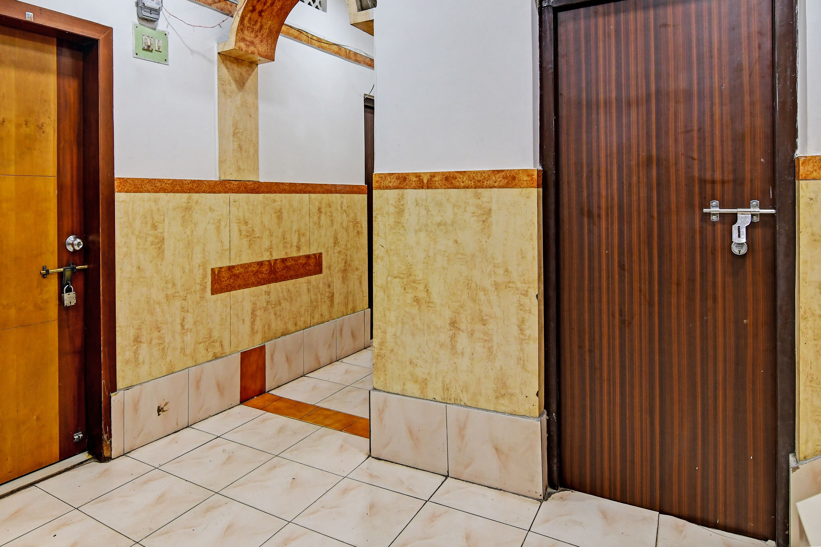 Un couloir carrelé, avec une porte en bois sur la gauche et une porte marron sur la droite.