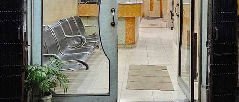 A hotel entrance with a reception desk, a waiting area with chairs, and a potted plant.