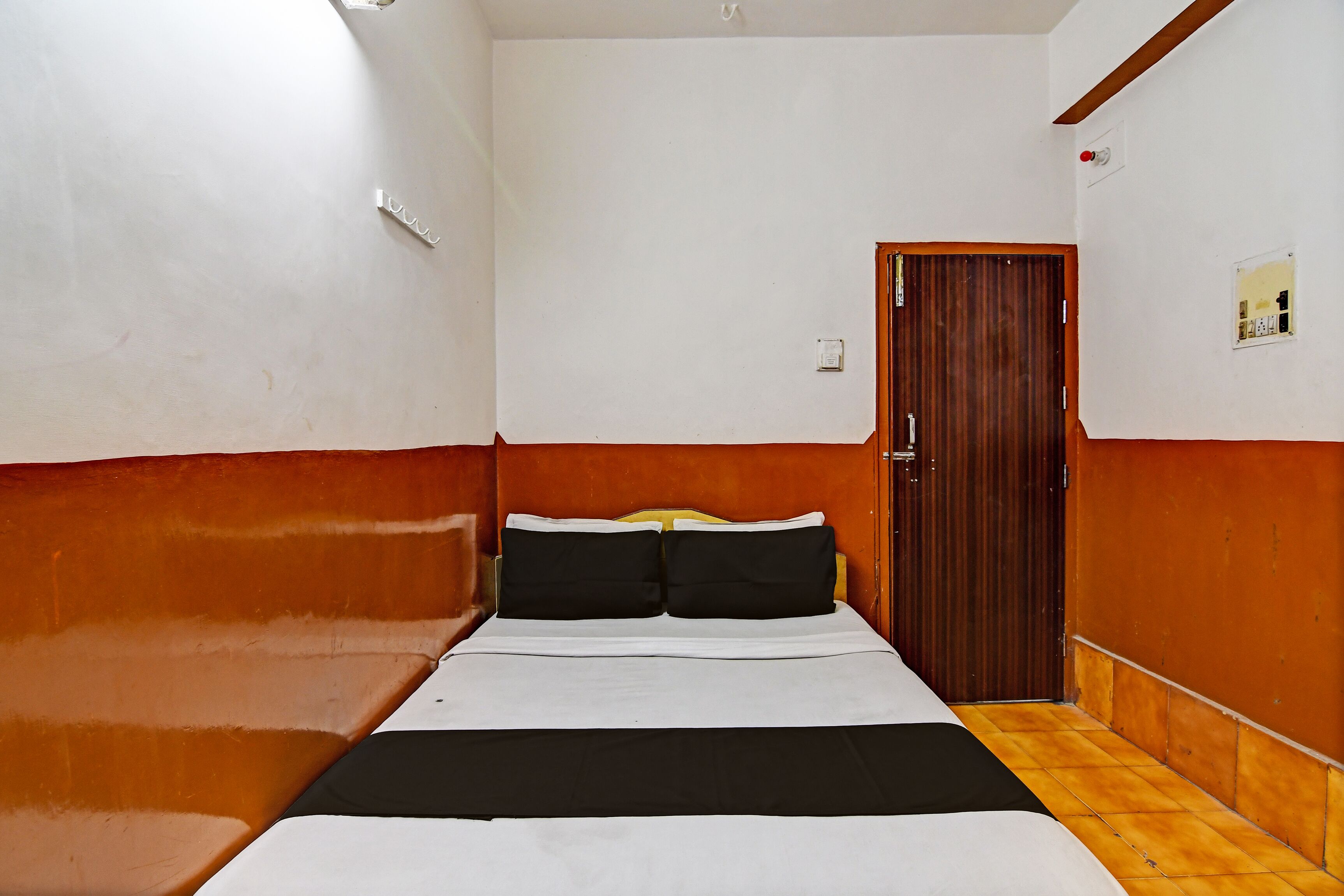 A hotel room with a bed, wooden floor, white walls, and a wooden door.