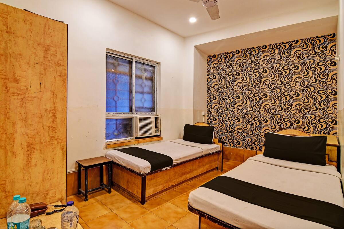 A room with two beds, a window with air conditioning, a patterned wall, and a wooden partition.