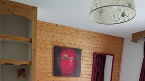 Ein Zimmer mit Holzvertäfelung, einem Bett mit Matratze, einem Stuhl, einem Kleiderschrank und einer Deckenleuchte.