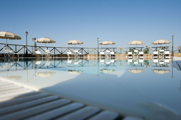 A pool with clear water reflecting the umbrellas and chairs.
