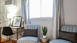 A modern living room with a desk, two armchairs, a small side table with a plant, and a window with curtains.