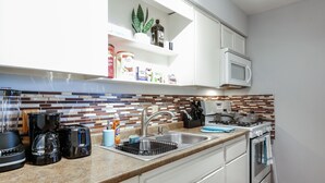 A modern kitchen with white cabinets, a stainless steel sink, a microwave, and a stove.