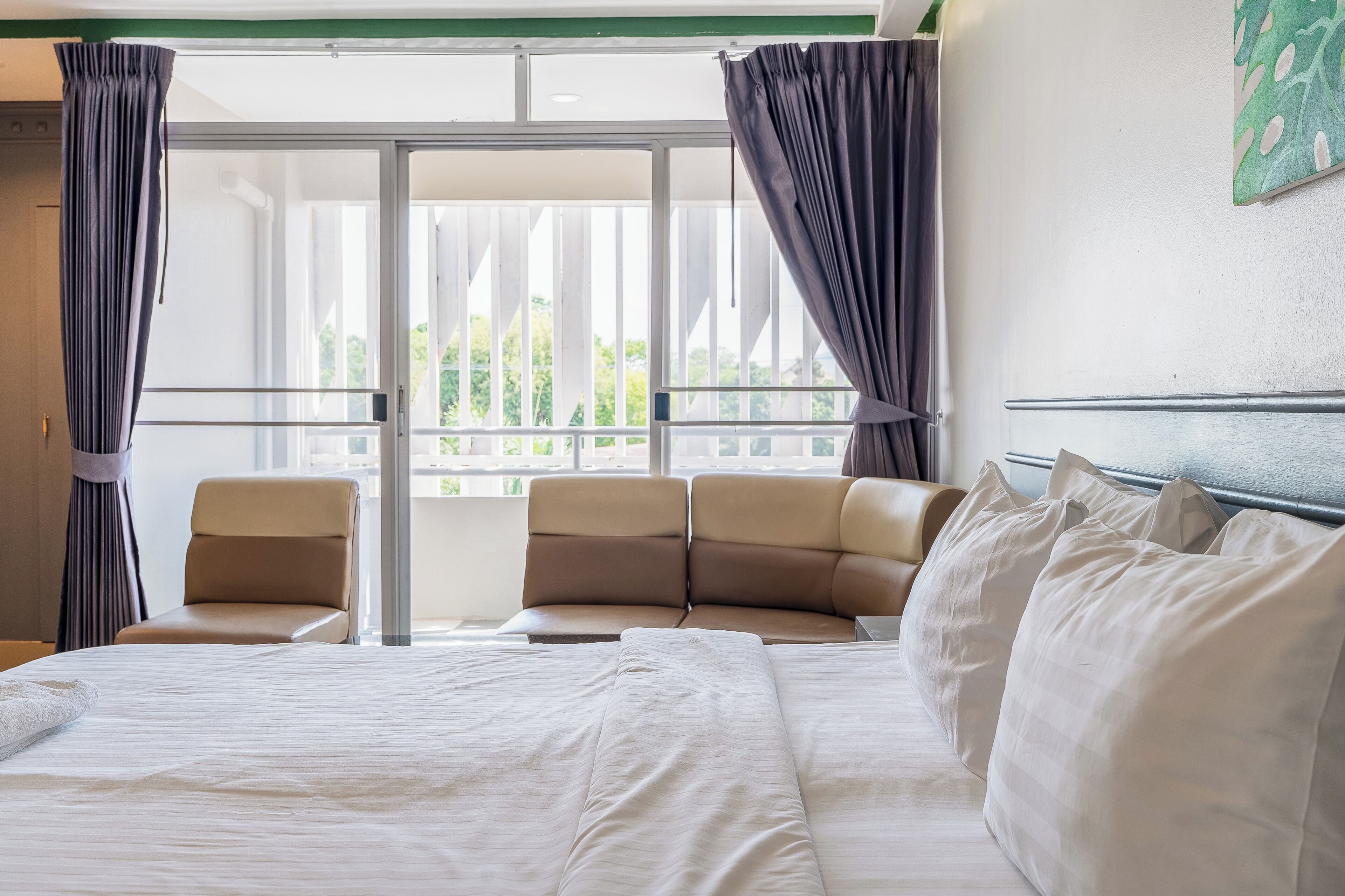 Habitación de hotel con cama, dos sillas, balcón con cortinas y vistas a vegetación.
