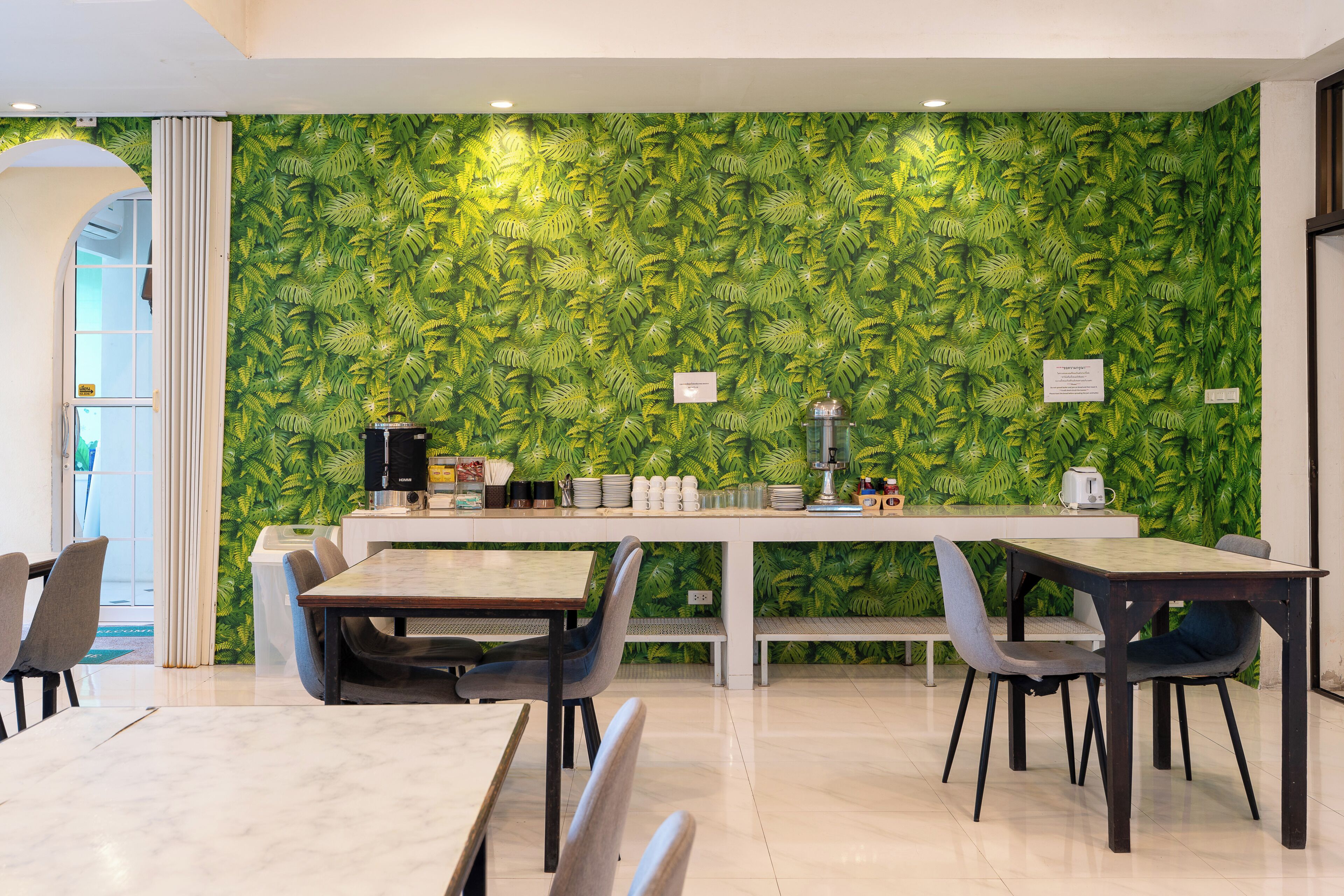 A modern dining area with a green leaf-patterned wall, a long table, and several chairs.