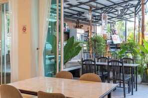 An indoor dining area with tables and chairs, a fan, and potted plants.
