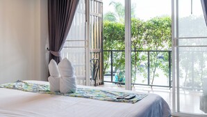 A hotel room with a bed, a window with curtains, a balcony, and a view of greenery. - Xanadu Hotel (Ban Chang)